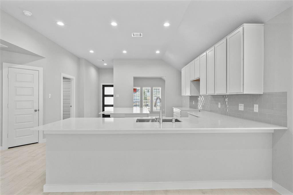 This stunning kitchen displays stained cabinets, custom neutral paint, quartz countertops, light modern backsplash, oversized kitchen island with extra storage, breakfast bar, recessed lighting, high ceilings and pantry.