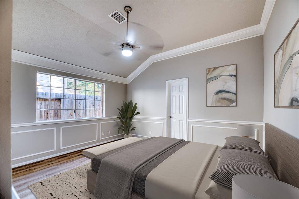 This primary bedroom features elegant wainscoting, a large window for natural light, and a ceiling fan. It has a neutral color scheme with modern accents and a cozy atmosphere.