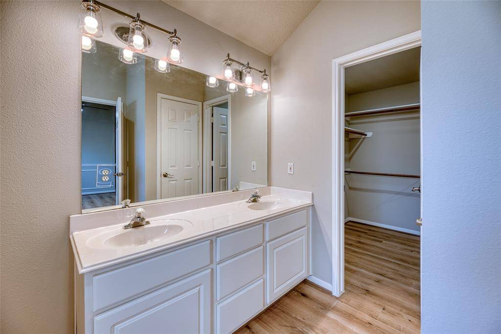 Ensuite bathroom features a double sink vanity, large mirror, and stylish lighting. It leads into a spacious walk-in closet with ample shelving and hanging space.