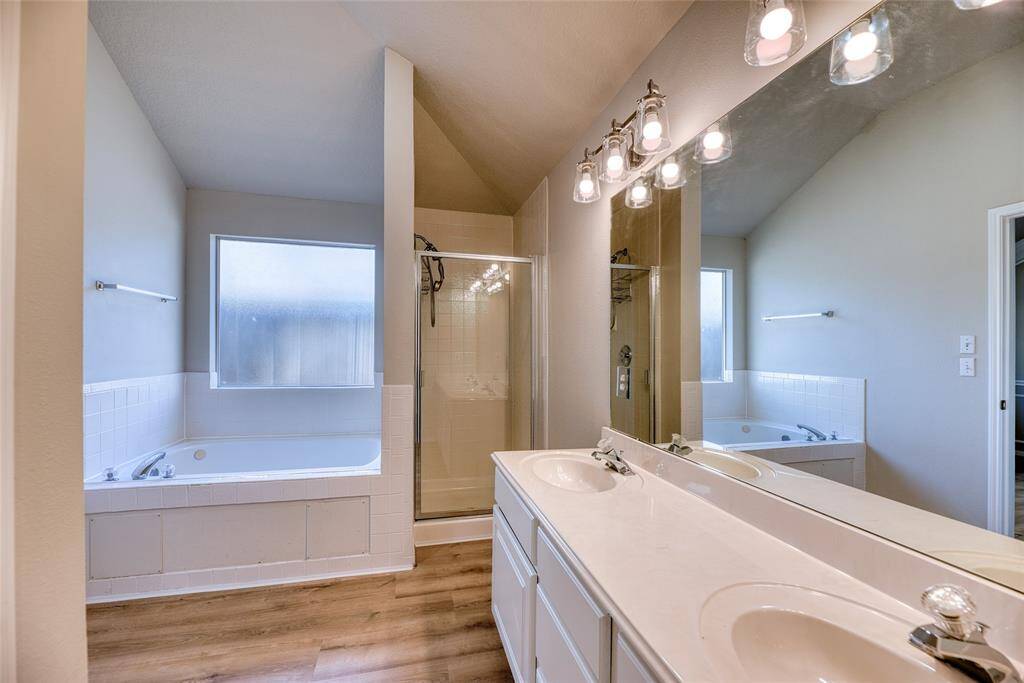 Bright bathroom featuring a double vanity with large mirrors, a glass-enclosed shower, and a spacious bathtub beneath a frosted window.