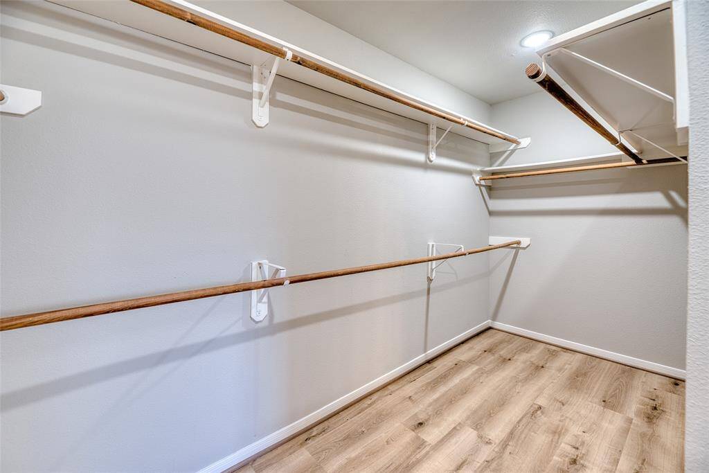 Spacious walk-in closet with multiple wooden rods for hanging clothes is ideal for ample storage and organization.