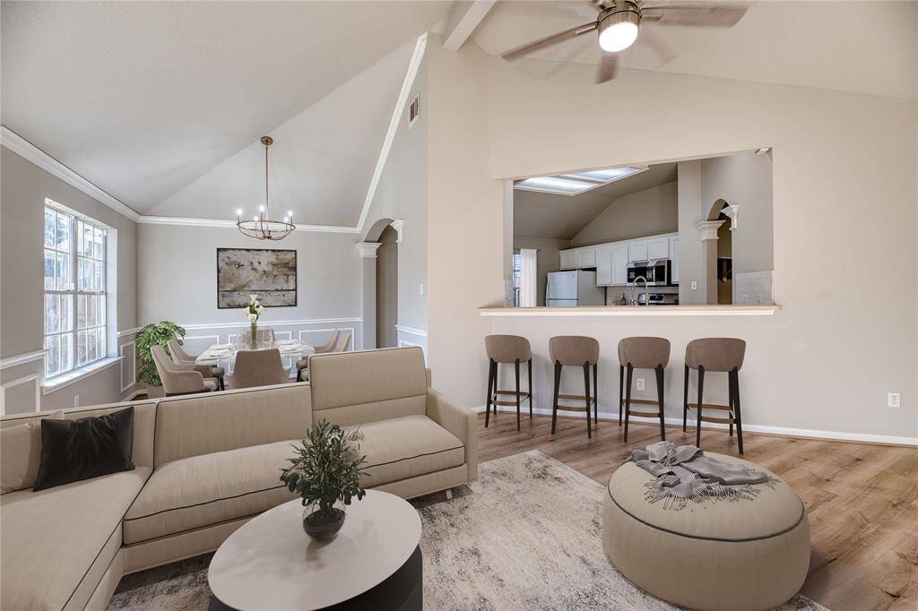 This inviting living space features high ceilings and a modern ceiling fan. It opens to a dining area with a stylish chandelier and abundant natural light.