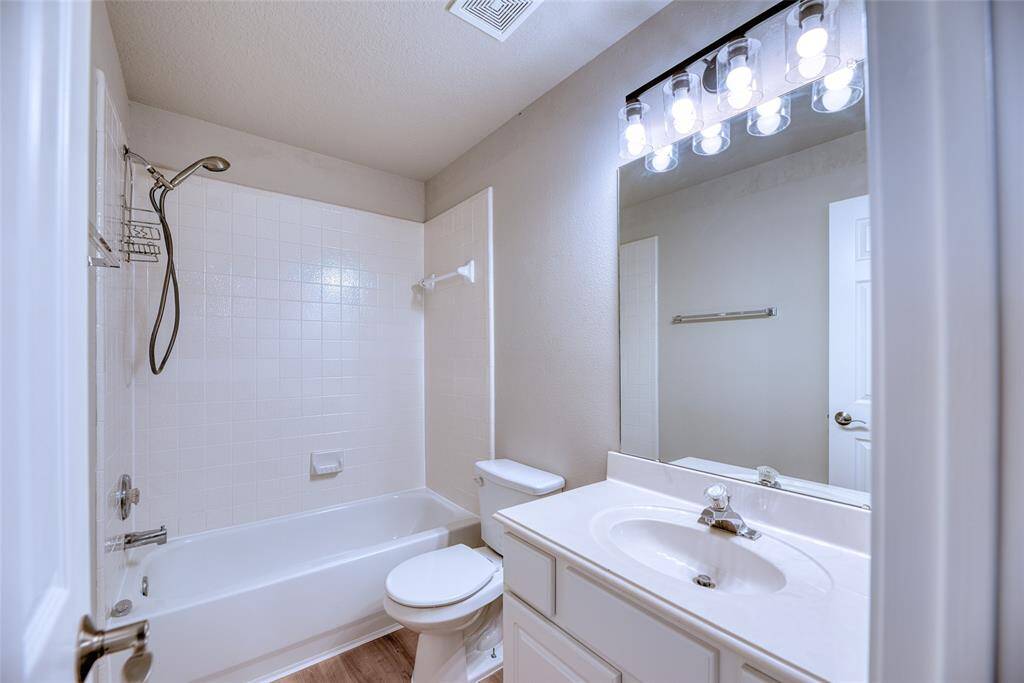 This bathroom features a clean, bright design with a shower-tub combo, a large mirror, and modern lighting. The vanity offers ample counter space, and the room is finished with neutral tones.