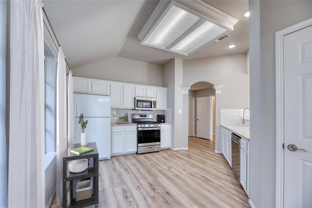 Bright and airy kitchen with modern appliances, white cabinetry, and light LVP flooring. Features a high ceiling with recessed lighting!