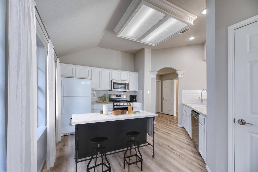 Modern kitchen with light flooring, white cabinets, and stainless steel appliances. Virtual staged island