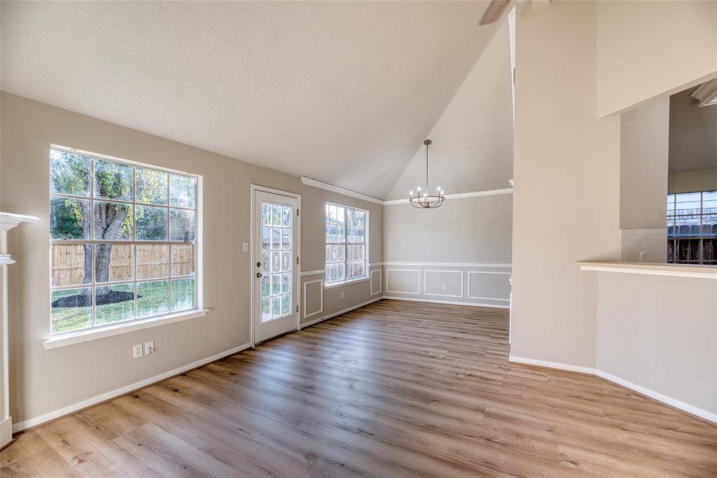 This bright, open living space features high ceilings, large windows, and elegant flooring. It has a modern chandelier, neutral walls, and access to a fenced backyard, perfect for natural light and outdoor views.