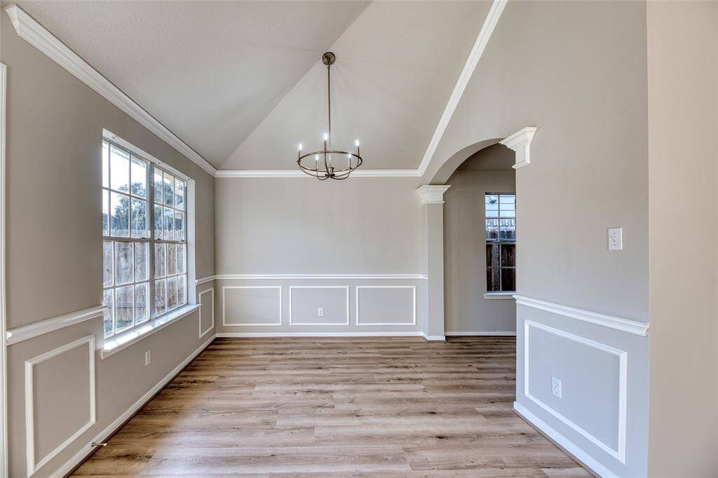 Bright dining room with vaulted ceiling and elegant chandelier. Features large windows and wainscoting, offering a spacious and inviting atmosphere.