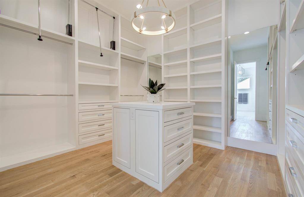 Primary closet is all custom built cabinetry on site. Features an island with quartzite counter, pull down rods, and beauitful lighting.