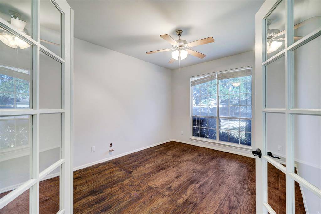 This room features large windows for ample natural light, elegant wood flooring, and a ceiling fan. It is accessed through stylish double glass doors, making it ideal for an office or study.