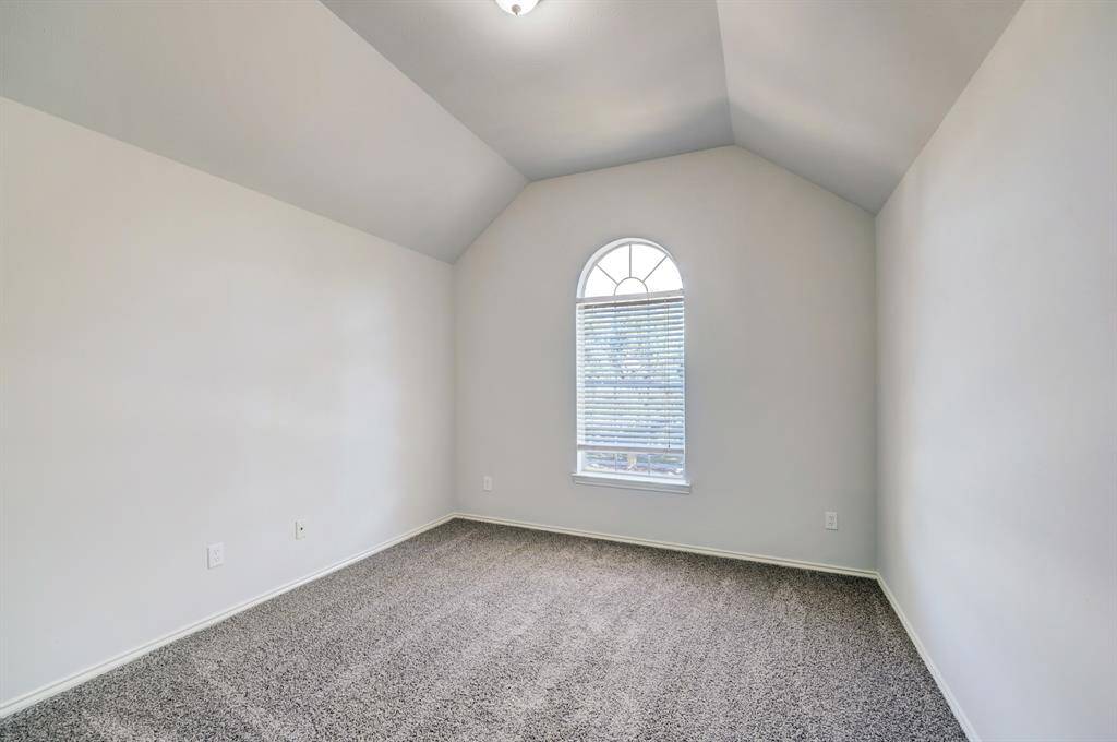 This room features a high, vaulted ceiling and a large arched window allowing natural light to fill the space. The walls are neutral, and the floor is carpeted, creating a cozy atmosphere. Perfect for a bedroom or office.