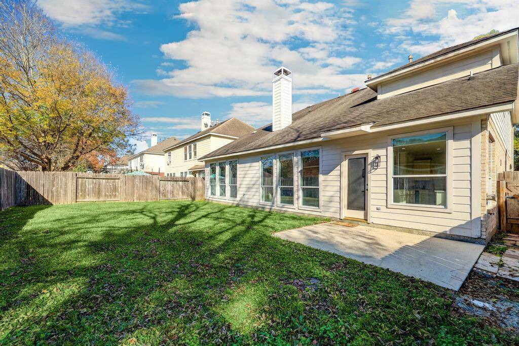 Charming backyard featuring a spacious lawn, mature tree, and a concrete patio, perfect for outdoor activities. The house has large windows for ample natural light, and a wooden fence offers privacy.
