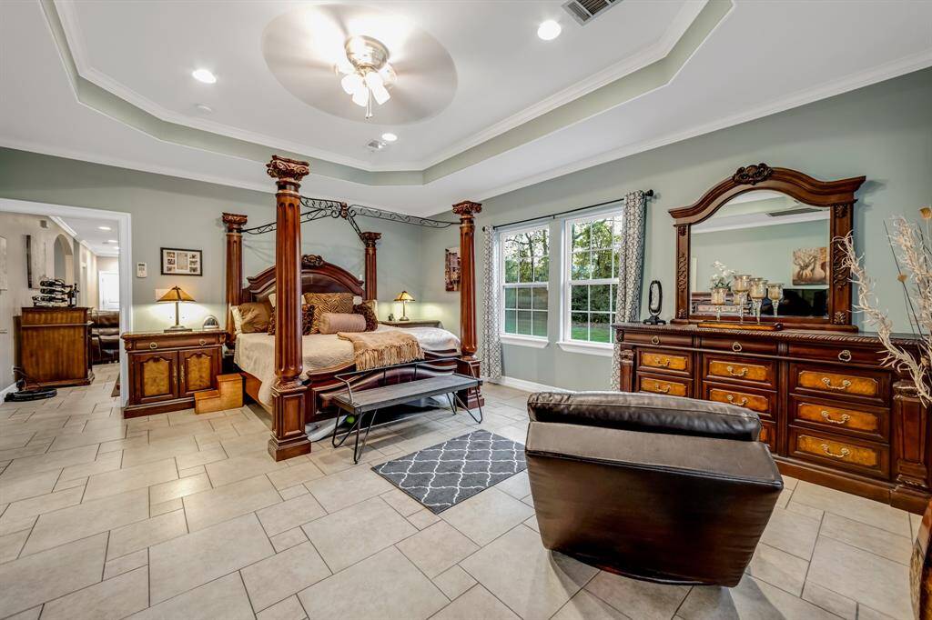 Another view of the owners retreat features a tray ceiling, crown molding, canister lights, ceiling fan with lights and patterned tile flooring