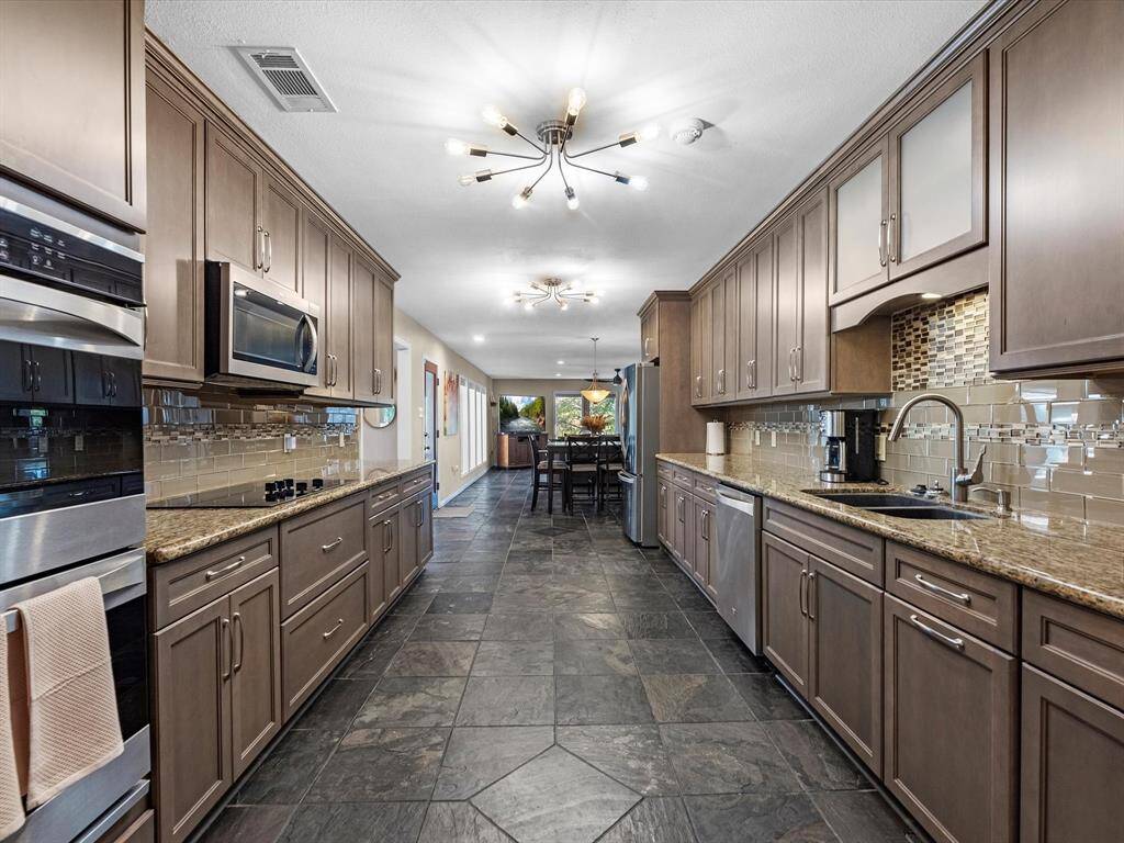 Beautifully updated oversized galley Kitchen complete with DOUBLE OVENS, Glass Cooktop, Granite Countertops, Custom Lighting, extended upper and lower cabinetry and countertops for extra storage and food prep space