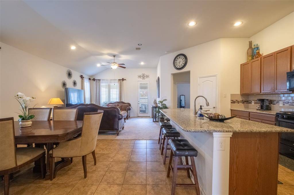 Open-concept living and dining area with a modern kitchen. It features a spacious layout, high ceilings, tile flooring, and a large island with bar seating. The living area has ample natural light.