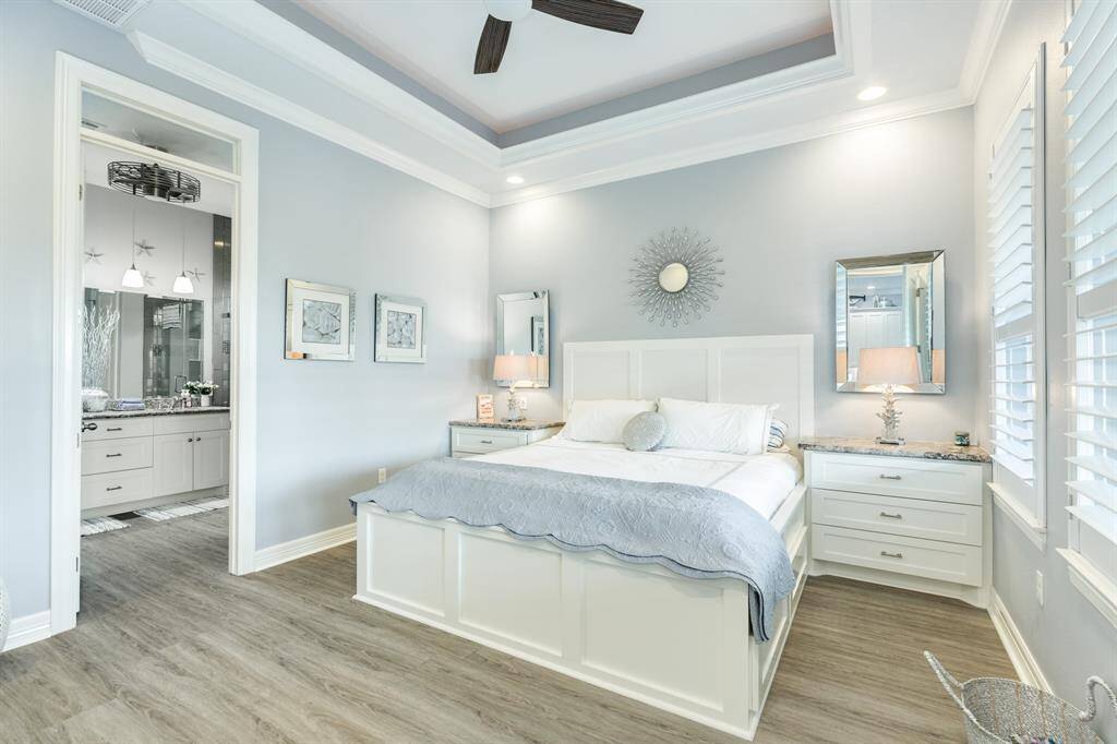 Primary bedroom with built in bedside cabinetry & bed frame with storage under, inset tray ceiling, plantation shutters and crown molding.