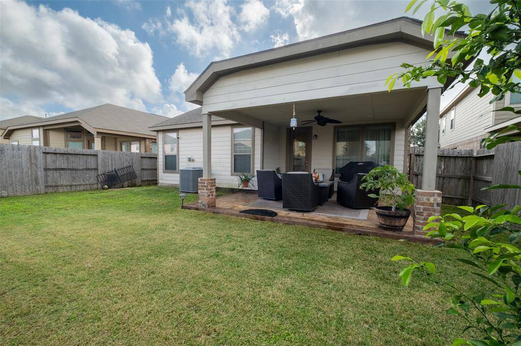 Cozy backyard with a covered patio, featuring outdoor seating and a ceiling fan. enclosed by Well-maintained lawn, ideal for relaxation and entertaining.