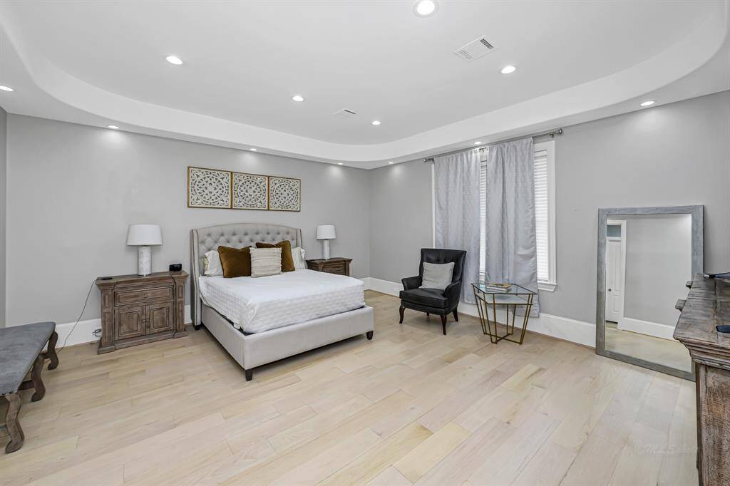 The large primary bedroom is a tranquil retreat that combines comfort, sophistication, and stunning views of the lush backyard and pool
