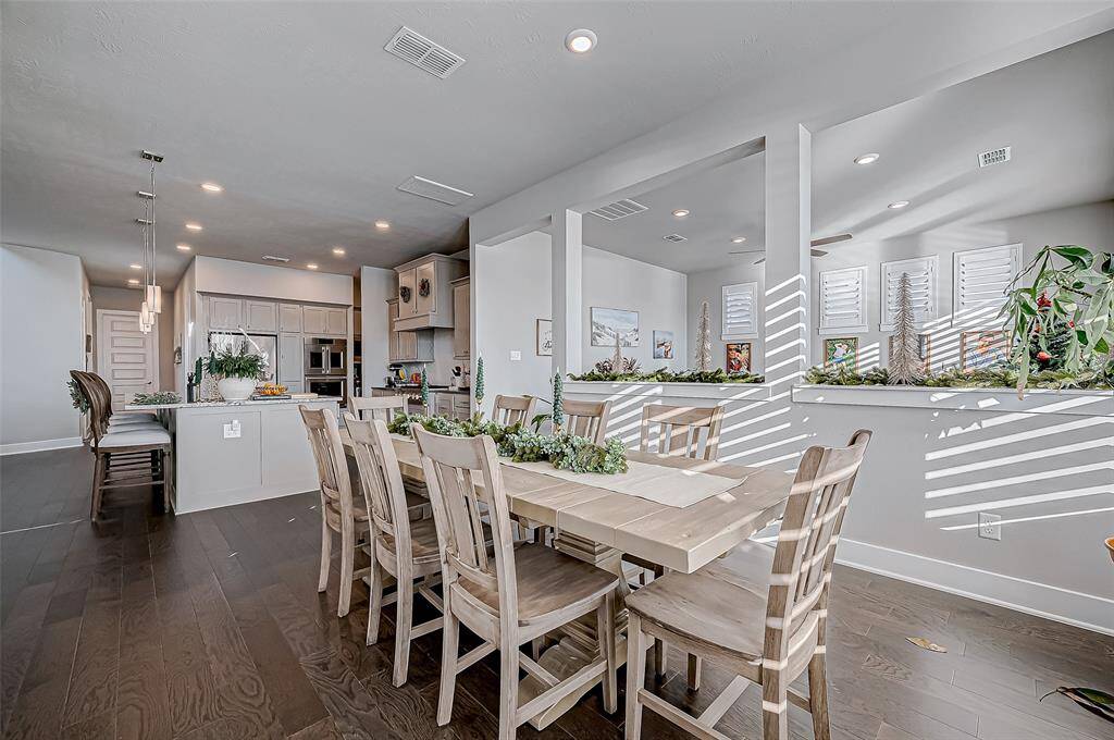 The photo showcases a spacious, open-concept dining and kitchen area with modern finishes. The kitchen features sleek cabinetry, stainless steel appliances, and a large island with bar seating. The dining area is bright and inviting, with ample natural light and attractive wood flooring, creating a warm and welcoming atmosphere.