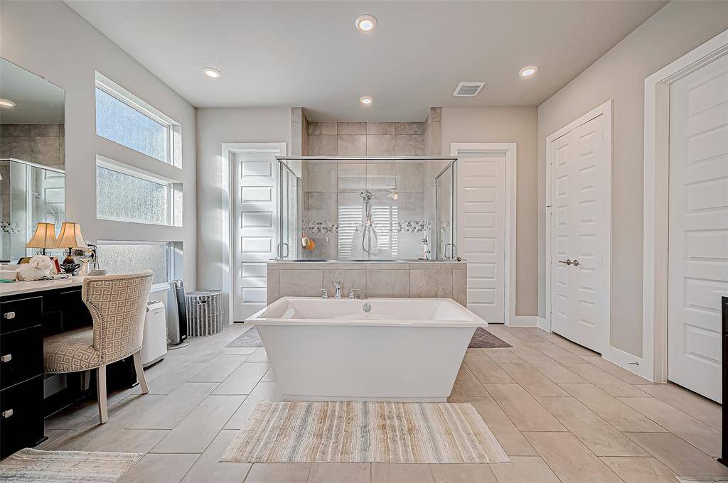 This photo showcases a spacious, modern bathroom featuring a freestanding tub, a large glass-enclosed shower, and double vanity with stylish fixtures. Natural light streams in through frosted windows, enhancing the elegant tile flooring and neutral color palette.