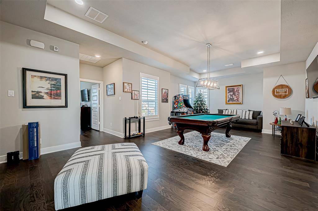 This spacious game room features a pool table, cozy seating area, and modern lighting. The room is bright with large windows, stylish decor, and dark hardwood floors, perfect for entertainment and relaxation.