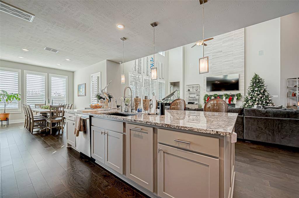 This open-concept living space features a modern kitchen with a large island, granite countertops, and sleek lighting. Adjacent is a dining area with ample natural light from large windows. The living room is cozy, with a stylish fireplace and a decorated Christmas tree, offering a warm and inviting atmosphere.