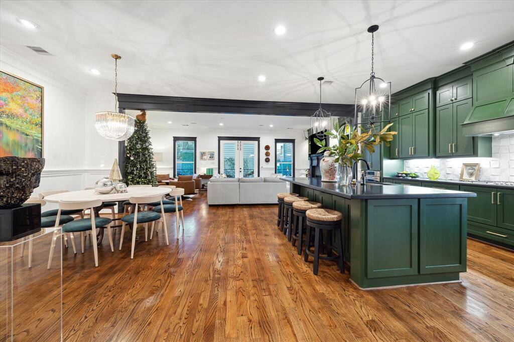 Spacious open-concept kitchen and living area with elegant green cabinetry and pendant lighting over the large island with bar seating. The dining area is highlighted by a modern chandelier.