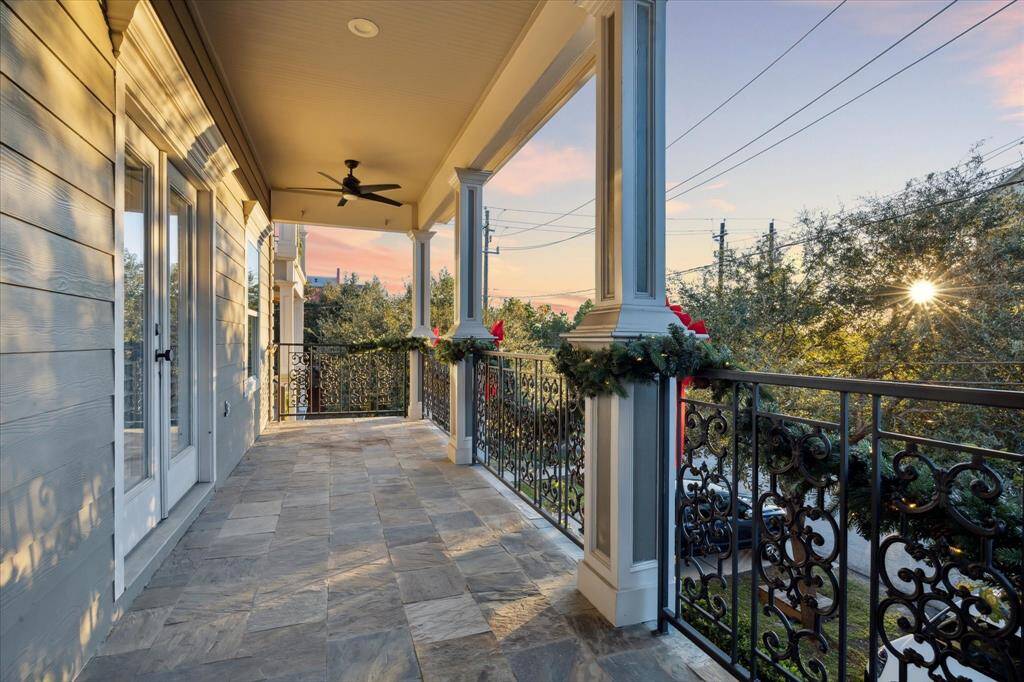 This spacious, covered porch with elegant wrought iron railings is located off of the primary suite. It features ceiling fans for comfort and a view of the front yard, perfect for relaxing or entertaining.