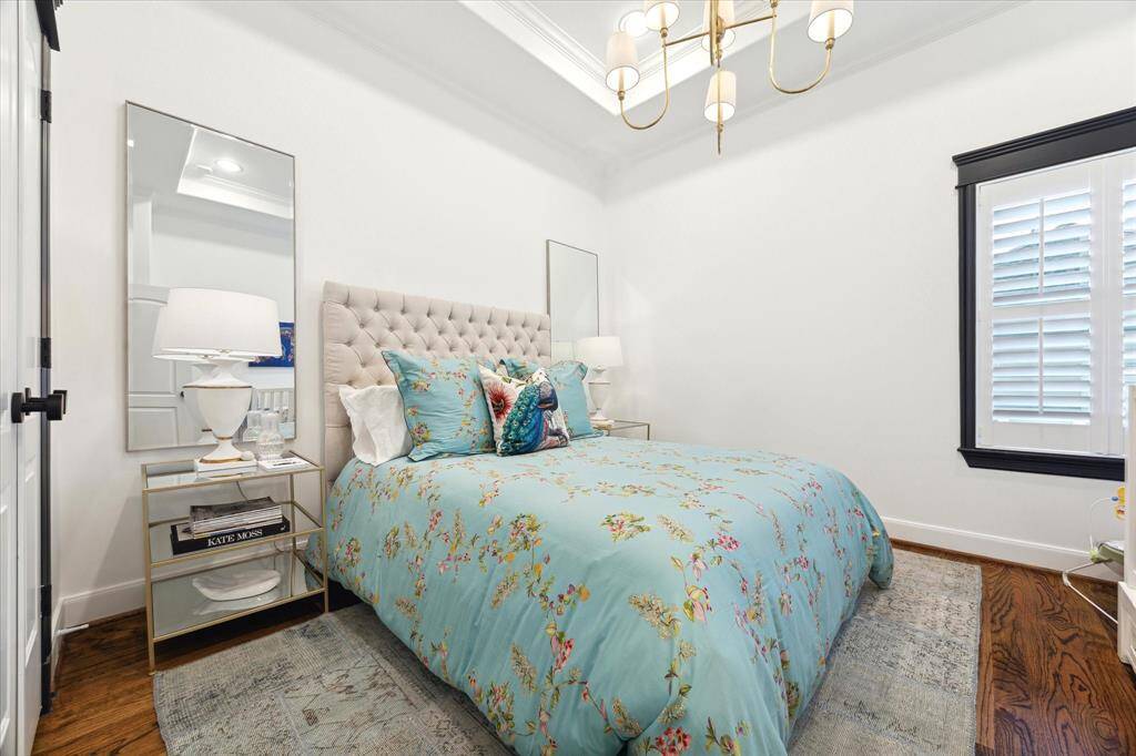 This second floor cozy bedroom features a queen sized bed with side tables.The elegant lighting, hardwood floors, and window with shutters, create a bright and inviting space.