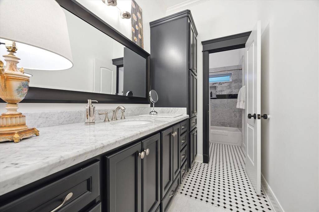 This second floor  bathroom features elegant black cabinetry with a marble countertop and dual sinks. The room is brightened by a large mirror and stylish lighting.