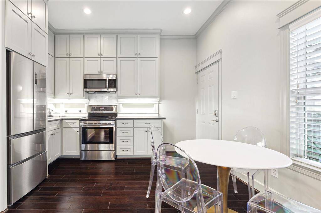 The garage apartment kitchen features stainless steel appliances, sleek white cabinetry, and a cozy dining nook. The dark wood floors add warmth and contrast, while ample natural light enhances the space's airy feel.