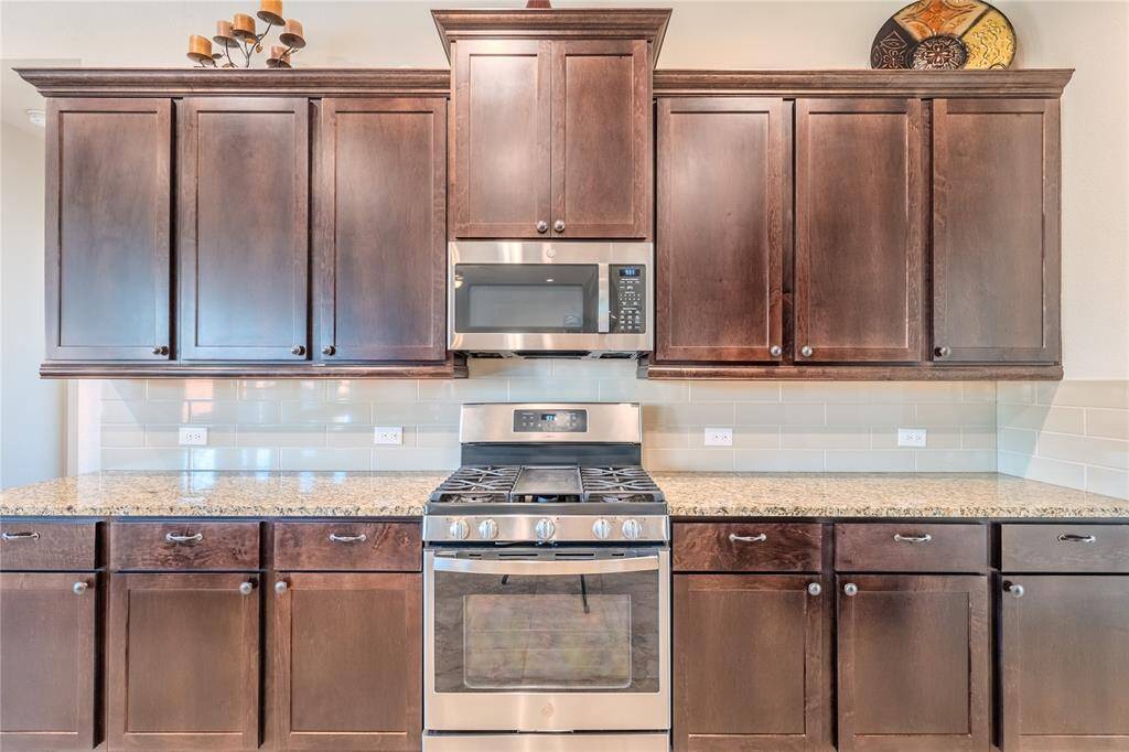 A modern gas stove and microwave are framed by a sleek tile backsplash and granite countertops, combining aesthetics with convenience