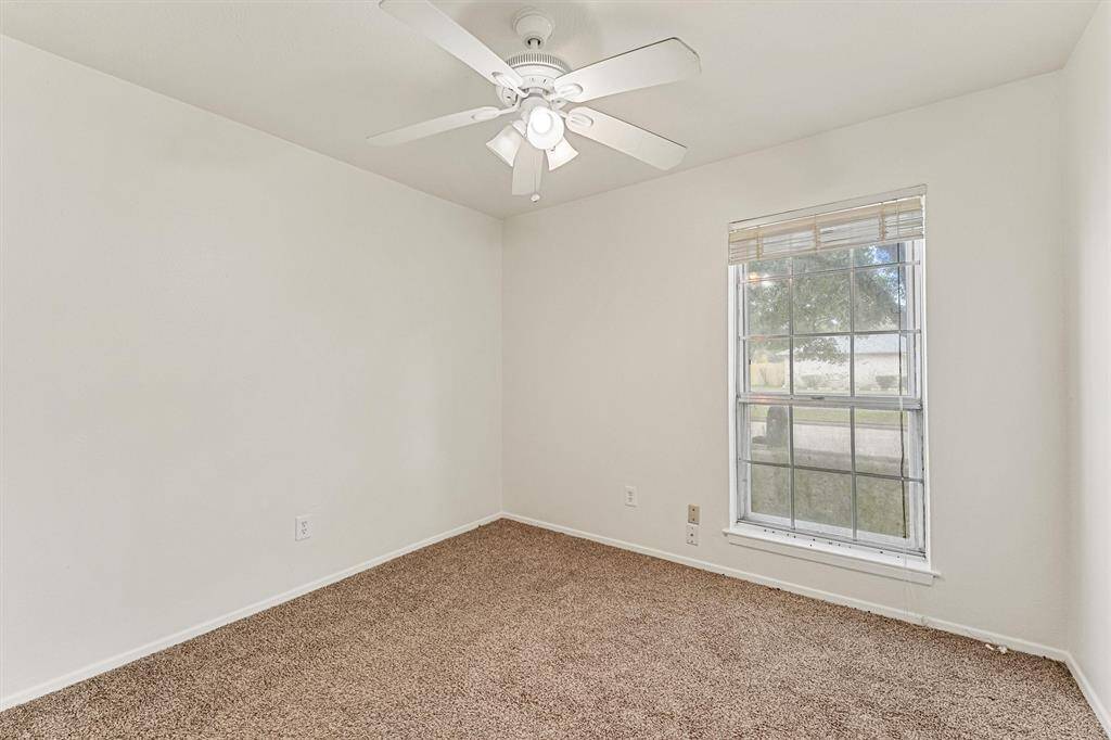 This room features neutral walls, a ceiling fan, and a large window providing natural light, with cozy carpet flooring. Ideal for a bedroom or home office.