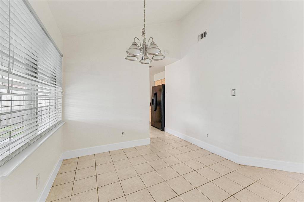 This photo features a bright dining area with tiled floors and large windows with blinds, offering plenty of natural light.