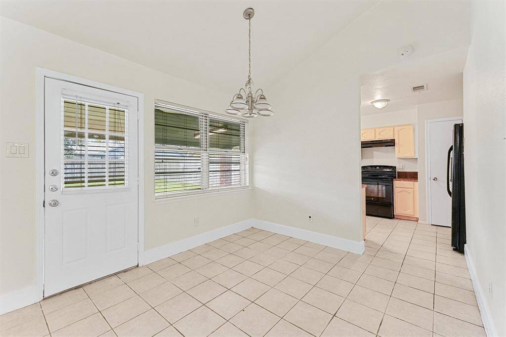 This bright dining area features tiled flooring and a large window with blinds, offering plenty of natural light. It opens to a cozy kitchen with light cabinetry and modern appliances.