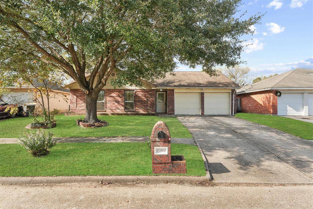 Charming single-story brick home with a two-car garage and a large front yard featuring a mature tree. The driveway offers ample parking.