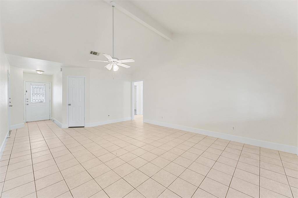 This spacious room features high ceilings, neutral tile flooring, and plenty of natural light. It includes a ceiling fan and offers an entryway with a decorative glass door, ideal for a bright and airy living space.