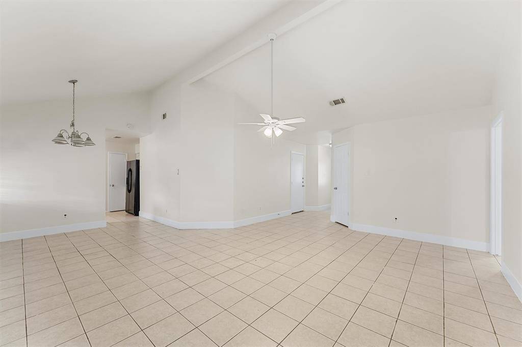 This spacious, open-concept living area features neutral tile flooring, high ceilings with a ceiling fan, and ample natural light. The area includes a dining space and connects to the kitchen, providing a versatile layout for comfortable living and entertaining.