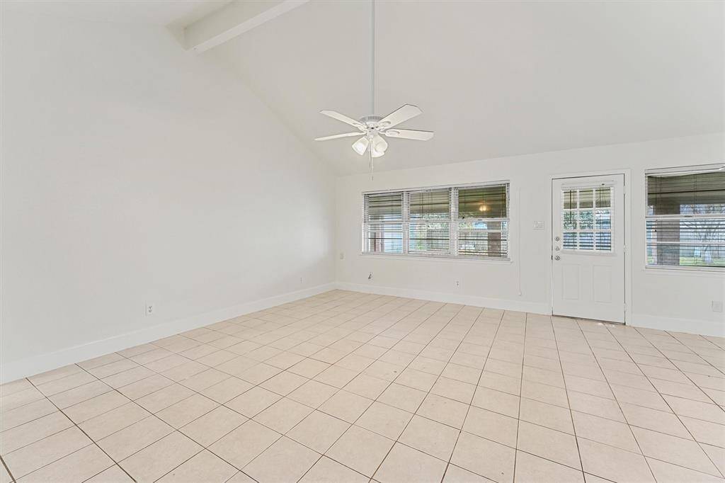 This spacious, bright room features high ceilings, neutral tile flooring, and ample natural light from large windows. The ceiling fan adds comfort, and a door provides easy access to the covered patio.