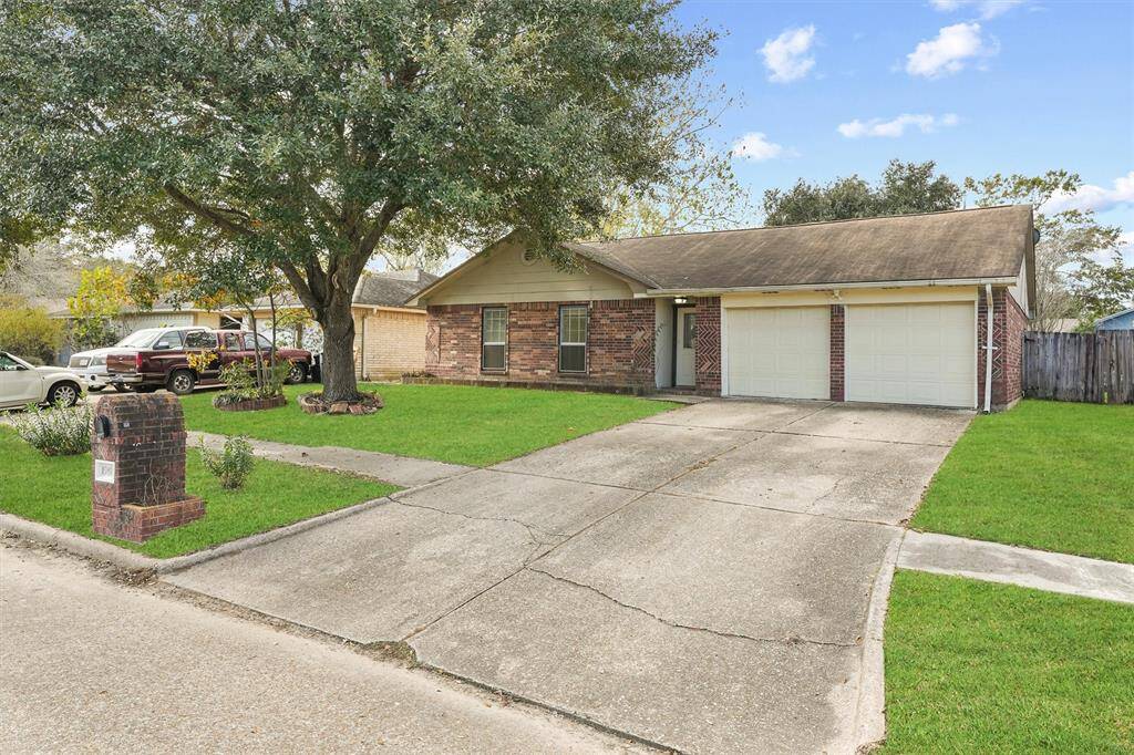 This charming single-story brick home features a two-car garage, a spacious driveway, and a well-maintained front lawn with a large shady tree.