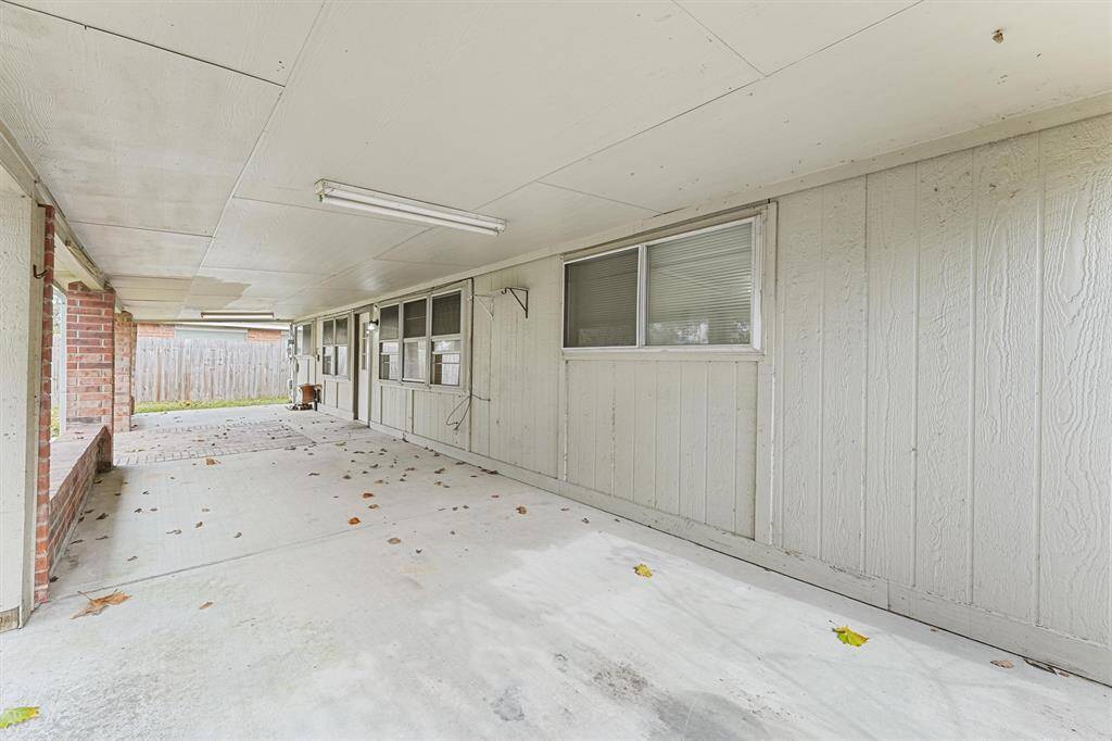 This photo shows a spacious covered patio with a concrete floor and panel siding, featuring large windows for natural light. The area is ideal for outdoor gatherings and has a brick accent wall, leading to a fenced backyard.