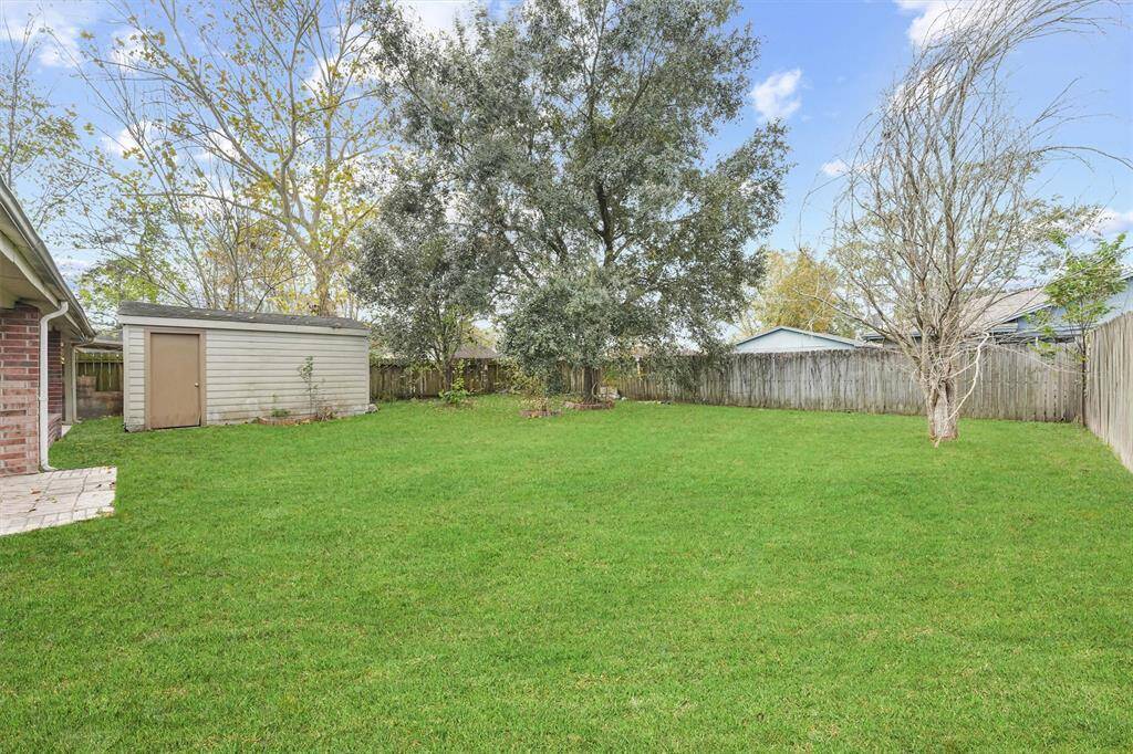 Spacious backyard with a well-maintained lawn, mature trees, a wooden fence for privacy, and a small storage shed. Ideal for outdoor activities and gardening.