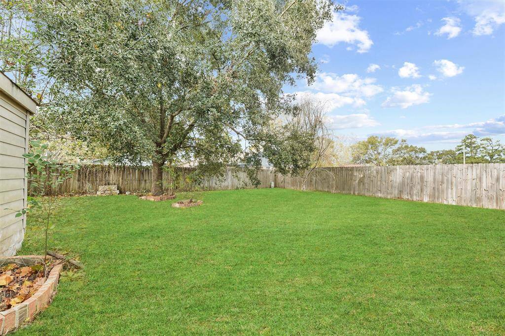 Spacious backyard with lush green lawn, mature trees, and a wooden fence providing privacy. Ideal for outdoor activities and relaxation.