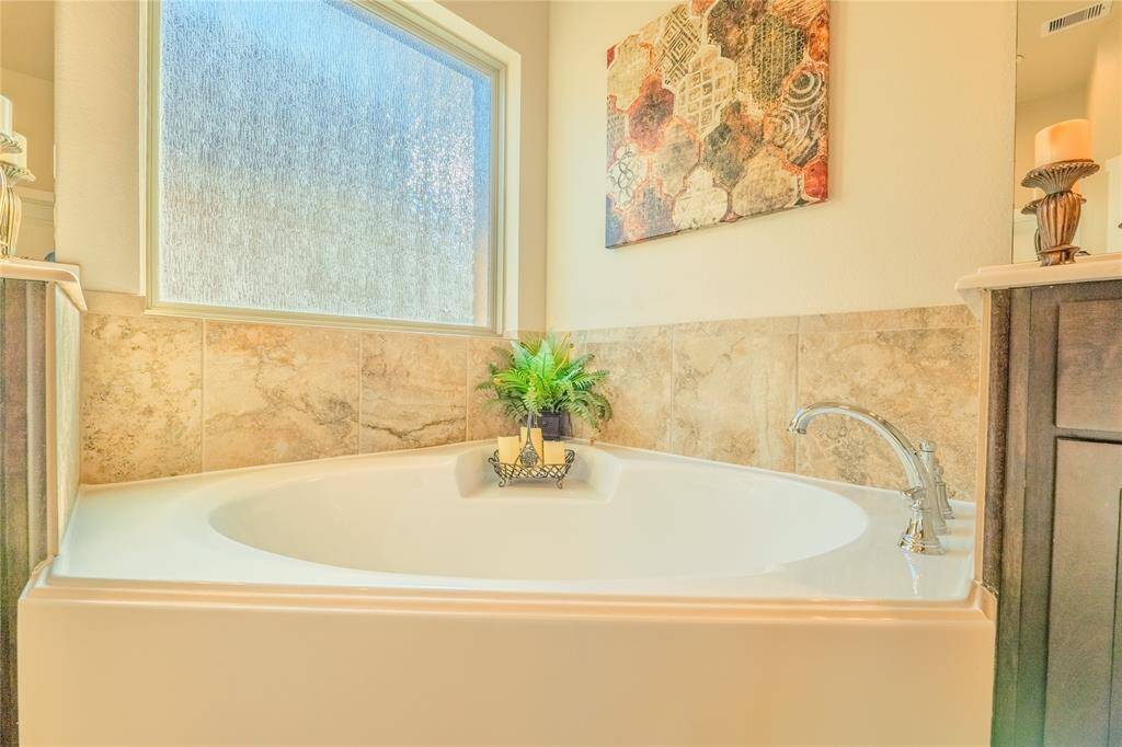 The luxurious primary bathroom features a relaxing garden tub with elegant tile surround, offering a serene space to unwind and soak in natural light from the frosted window above.
