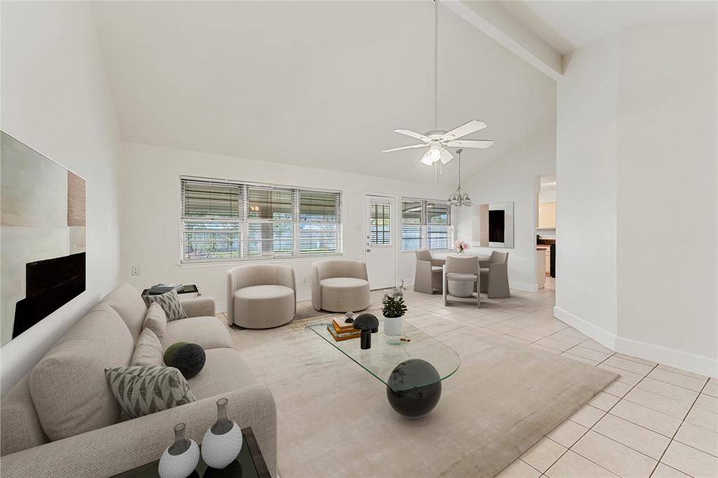 Virtually staged* This spacious room features a high vaulted ceiling, tile flooring, and ample natural light from large windows. A ceiling fan and light fixtures add functionality, and the neutral tones offer a versatile space for any decor style.