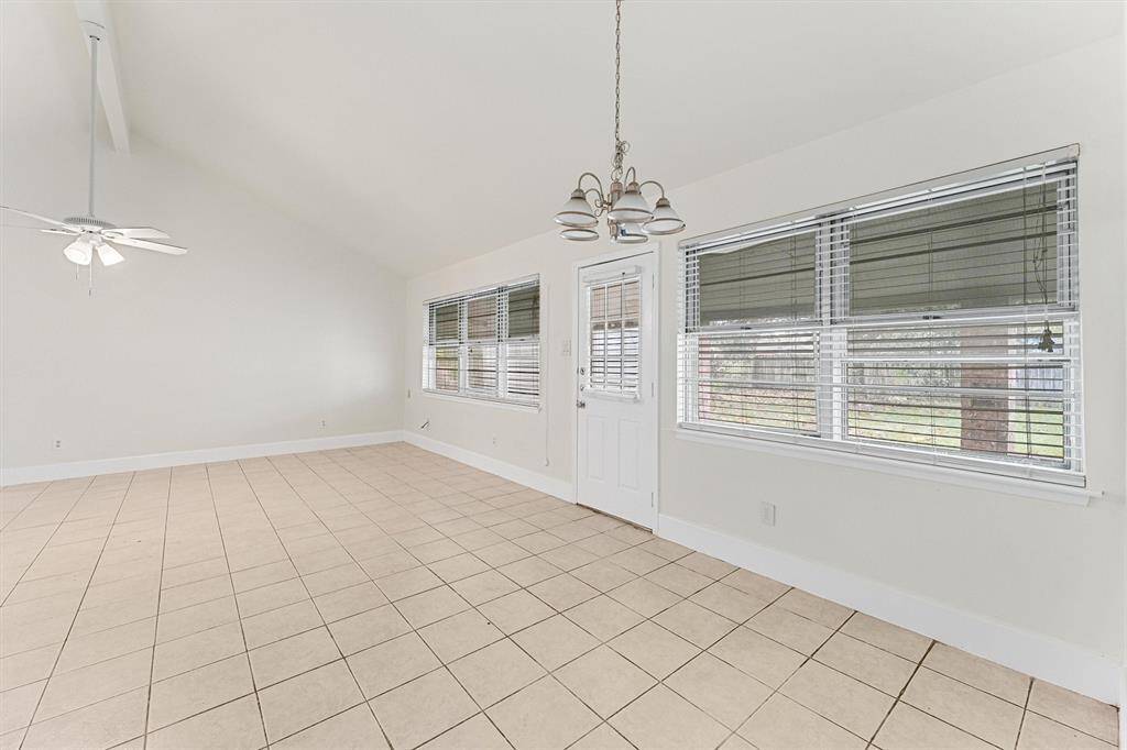Bright, spacious room with vaulted ceilings, tile flooring, large windows, and a ceiling fan, perfect for a versatile living or dining area.
