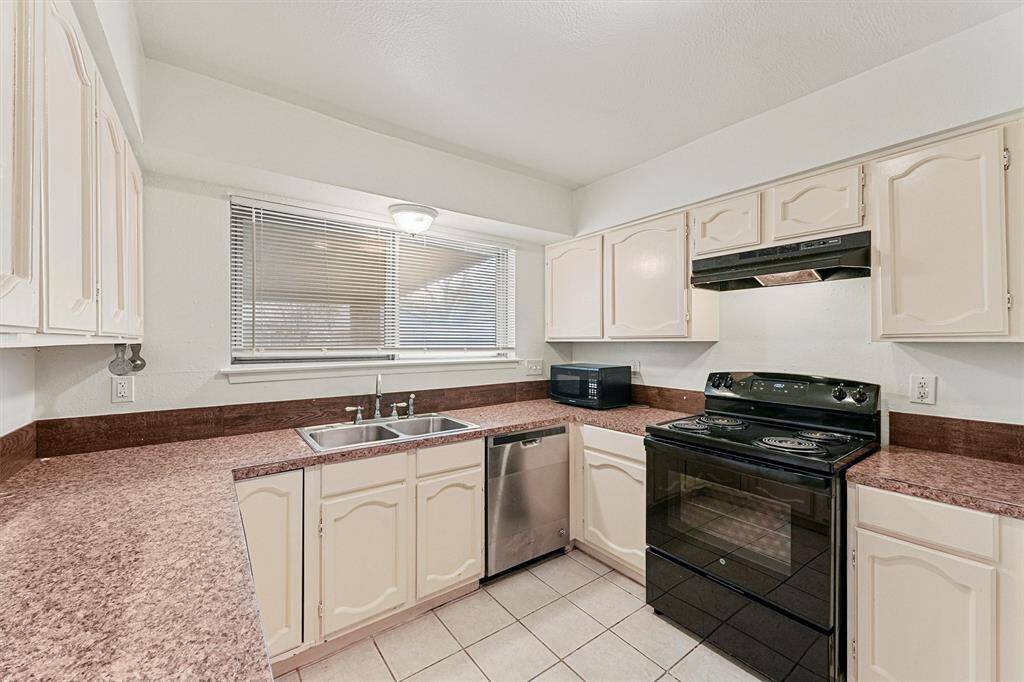 Bright kitchen with ample counter space, featuring light cabinetry, a double sink, and modern appliances including a black stove and dishwasher.