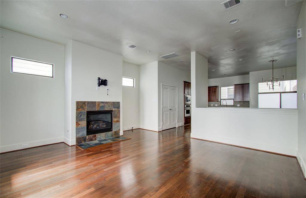 This spacious open-concept living area features hardwood floors, a modern fireplace, and a kitchen with a breakfast bar and contemporary lighting. Natural light streams through the high windows, creating a bright and inviting atmosphere.