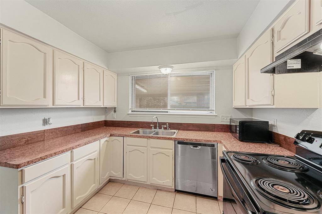 This kitchen features a double sink under a large window for natural light. It includes a black electric stove, a dishwasher, and a microwave.