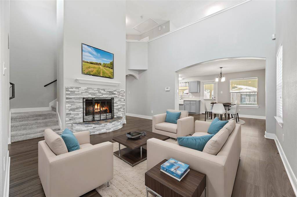 This chic sun-drenched living space with dramatic two-story ceilings, sleek wood-like vinyl planks, cozy fireplace, offers tons of charm for family and guests.