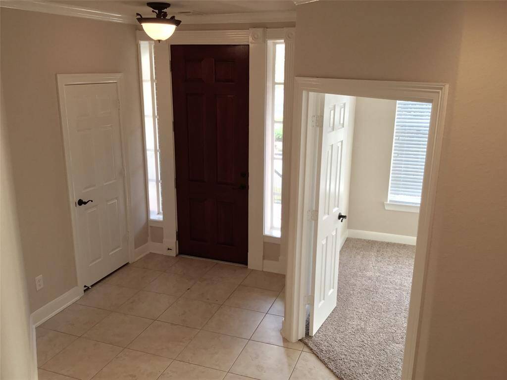 This entryway features a dark wooden front door with sidelights, tiled flooring, and leads to a carpeted room. It has a light fixture and neutral walls, creating a welcoming atmosphere.